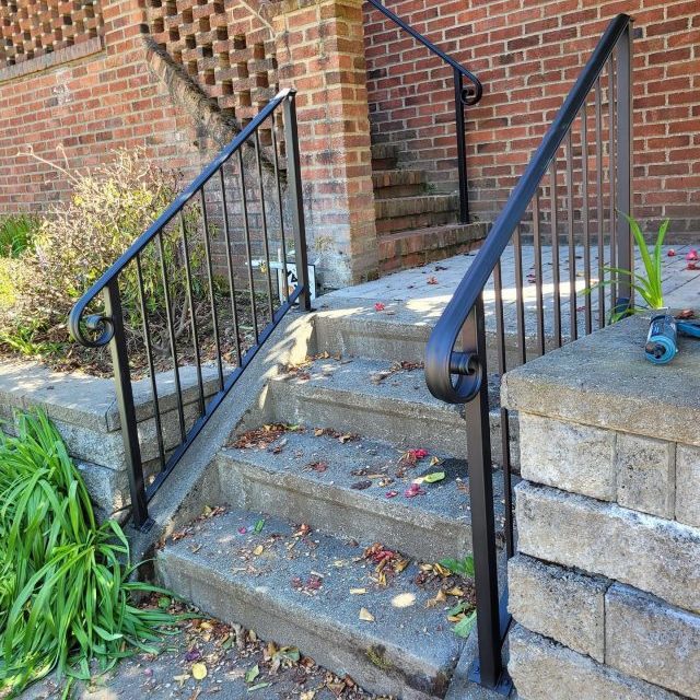 Black exterior stair railings with a lamb’s tongue handrail end and vertical bars.