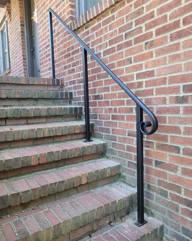 Black metal handrail with a curved lamb’s tongue end mounted on brick steps.