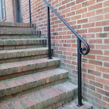 Black metal handrail with a curved lamb’s tongue end mounted on brick steps.