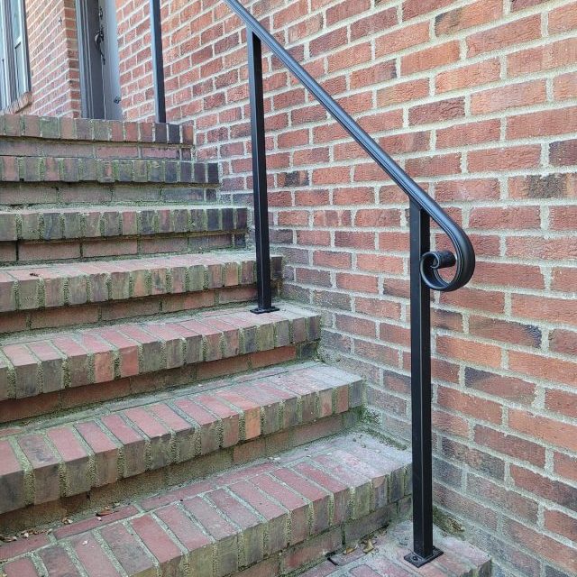 Black metal handrail with a curved lamb’s tongue end mounted on brick steps.