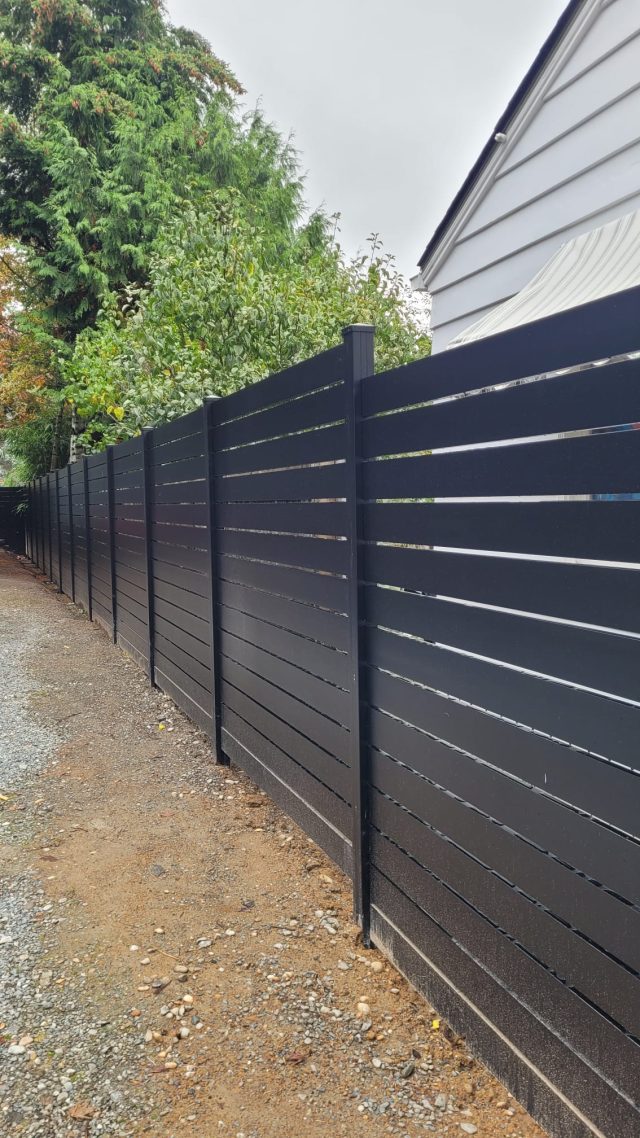 Black aluminum privacy fence with horizontal slats and gap spacing installed along a residential property.