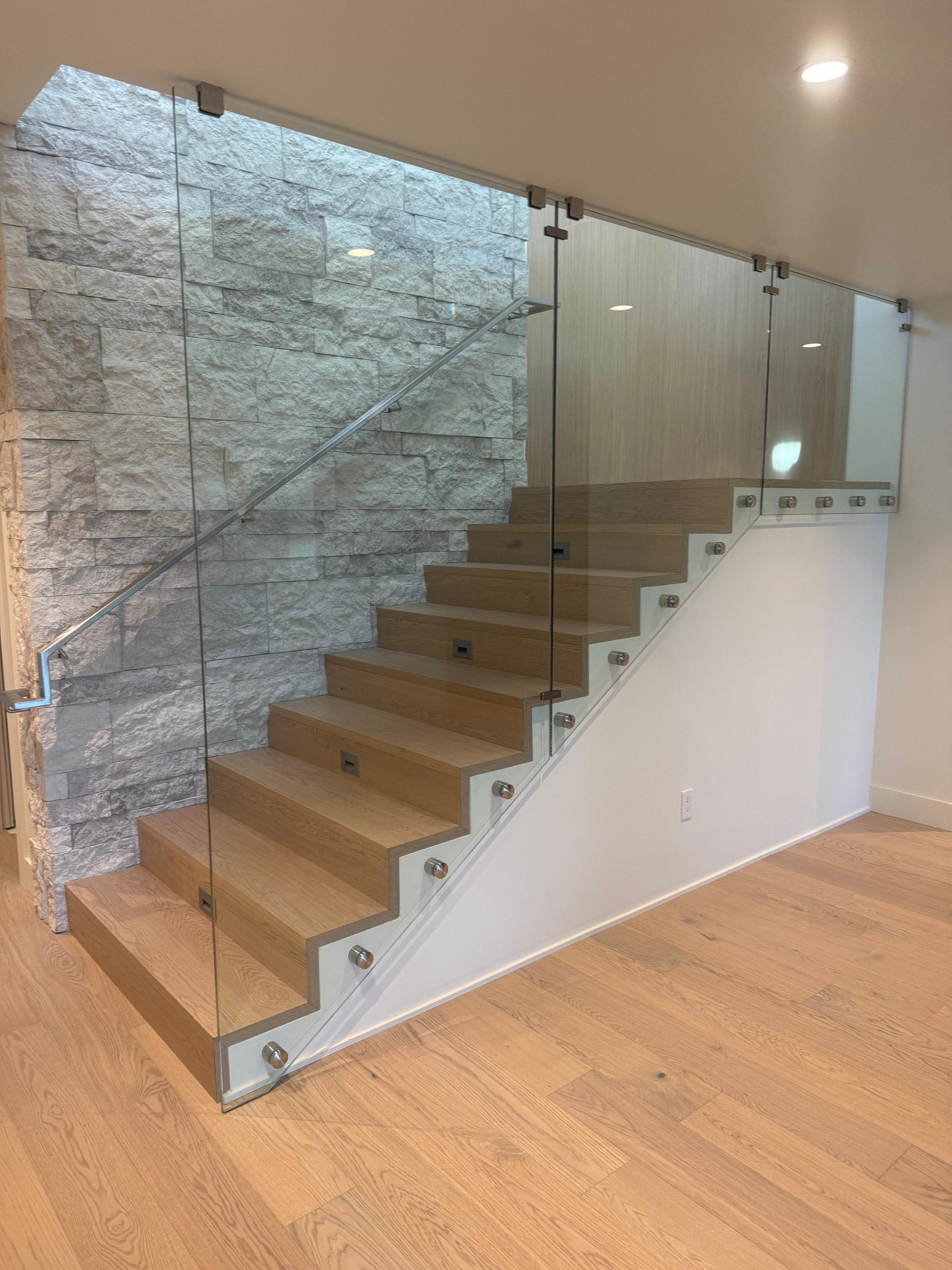 Interior staircase with tempered glass railings and stainless standoff mounts in a modern home