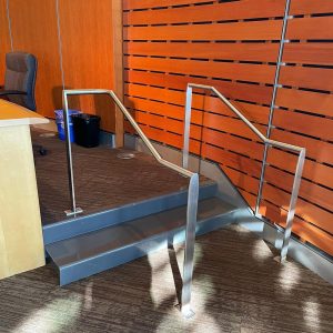 Brushed stainless steel commercial handrail system on interior steps with modern wall panels