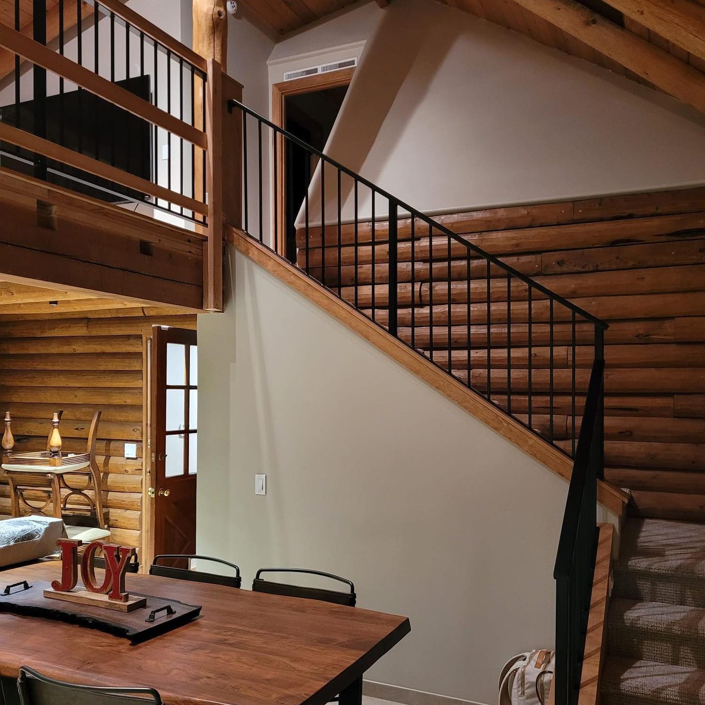 Rustic interior stair railing in a log home with wood handrail and black metal vertical balusters